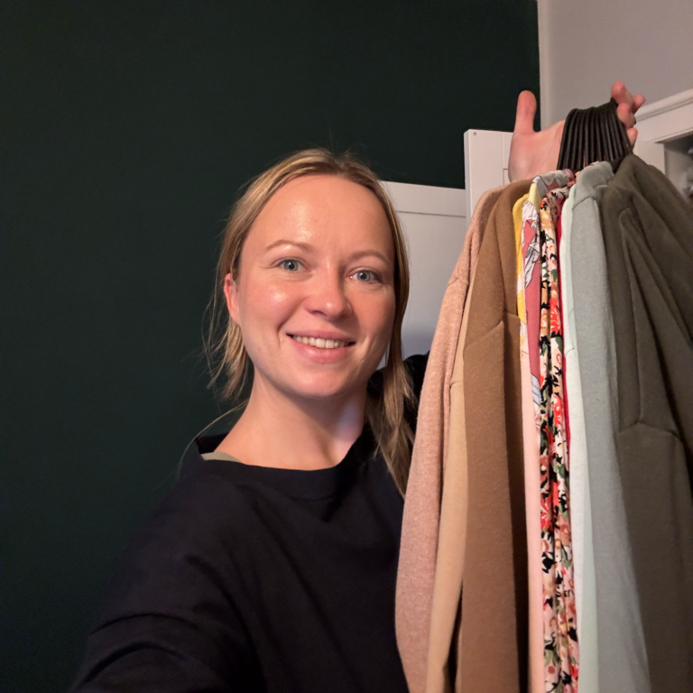 Eine lächelnde Frau hält eine Auswahl an Kleidung in der Hand.