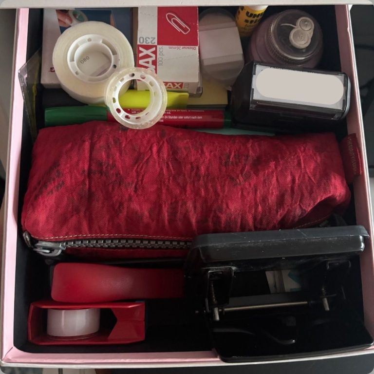 Schreibtisch-Box mit Bürobedarf wie Klebeband, Stiften und einem roten Etui.