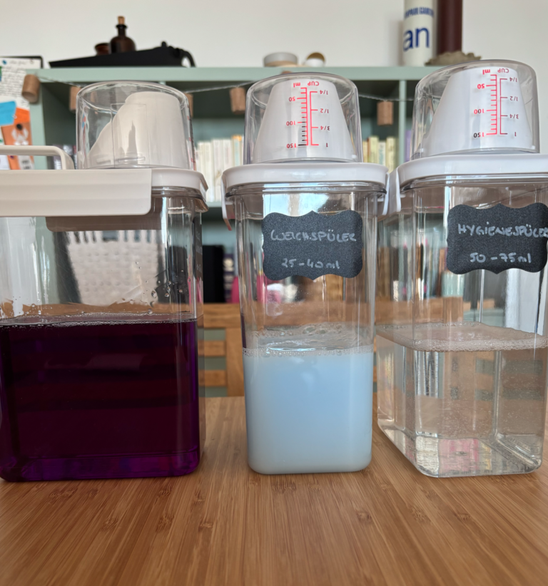 Drei transparente Behälter mit farbigem Waschmittelinhalt: lila, blau und klar.