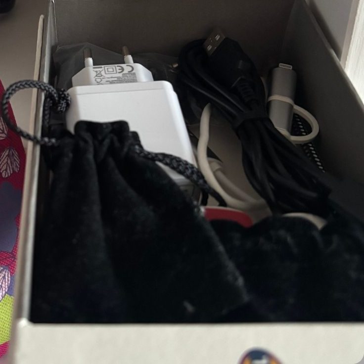 Weißes Ladegerät und verschiedene Kabel in einer Schachtel.