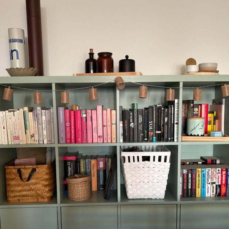 Bildausschnitt eines Regals in der orderly-Farbe "Salbei", das mit nach Farben sortierten Büchern und verschiedenen Körben gefüllt ist.
