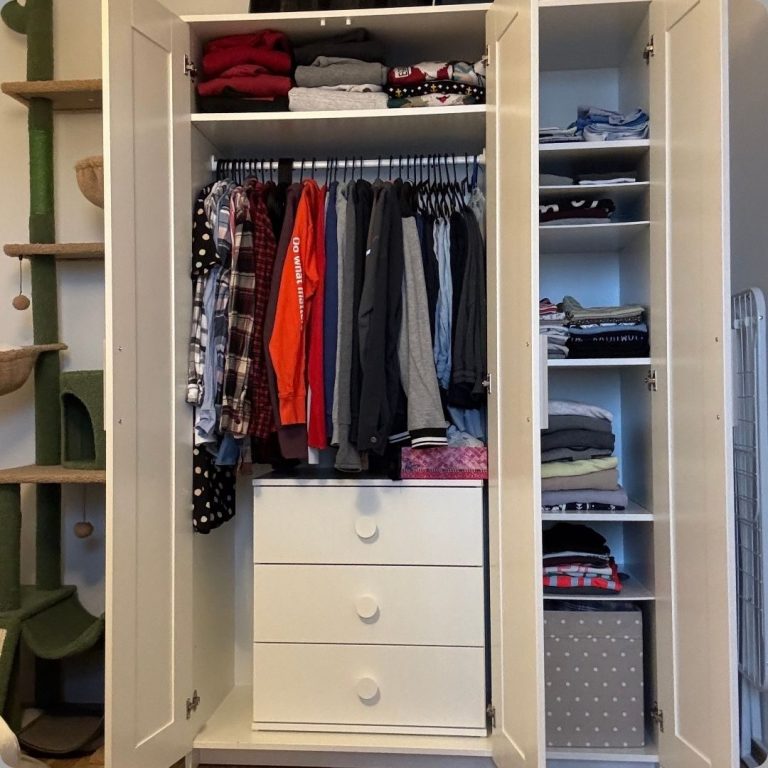 Offener Kleiderschrank mit Kleidung und Schubladen, daneben ein Regal mit fein säuberlich gestapelten Oberteilen.
